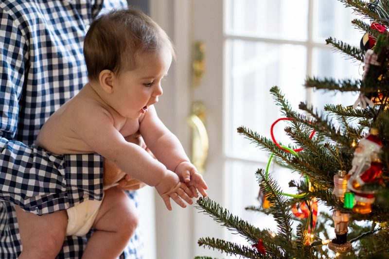 baby reaching for branches of Christmas tree in Connecticut