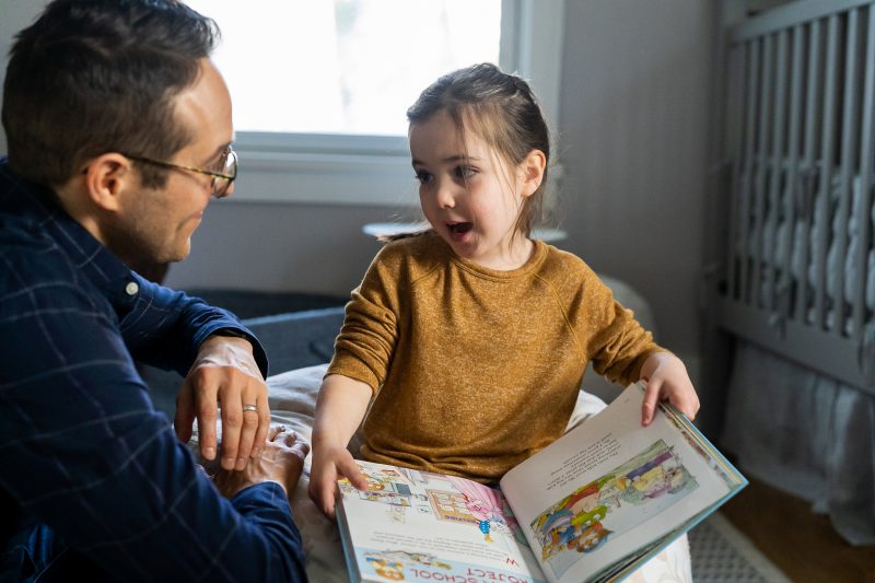little girl reading a picture book to her dad in her bedroom.  Maybe she's planning out her week? 