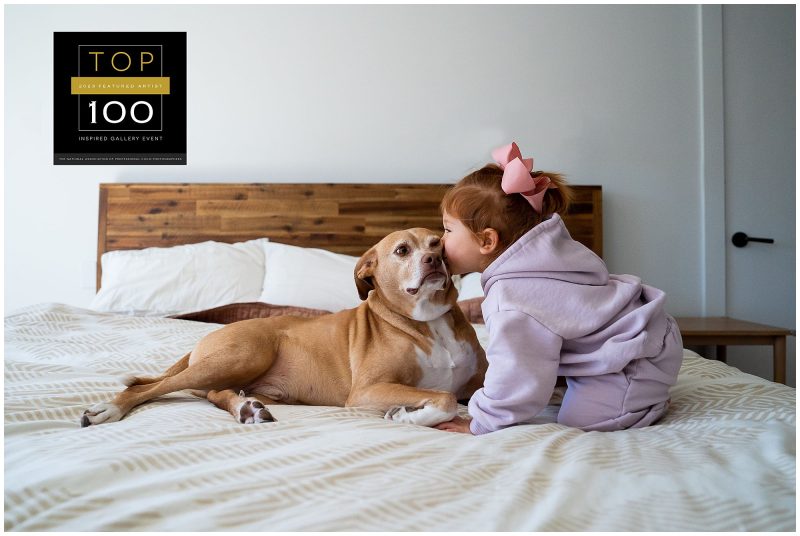 little red haired toddler kissing a dog's ear on a bed