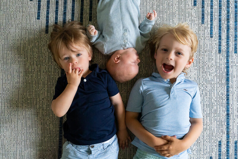 Two big brothers lying on the floor with their newborn baby brother.