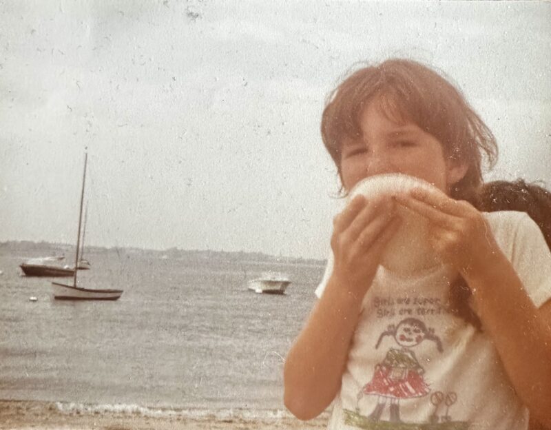 Little girl on the beach licking ice cream off a paper plate