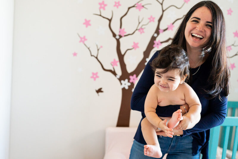 mom holding chubby baby in diaper near her crib in front of wall mural