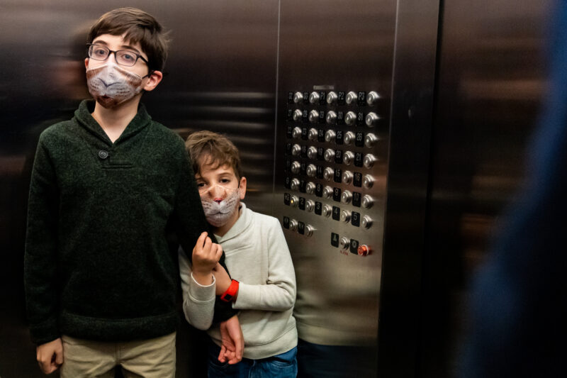 two little boys wearing masks in an elevator