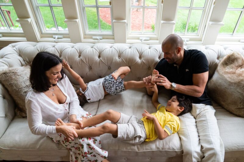 Family sitting on couch looking relaxed and smiling during a in home family photo session with Jaye McLaughlin