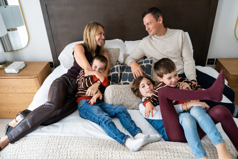 Family with three children relaxed on a bed during an in-home family travel photo session