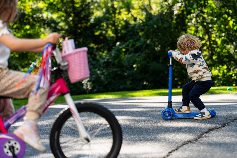 Young boy riding a scooter and a girl riding a bike in the backyard during a family photo session.