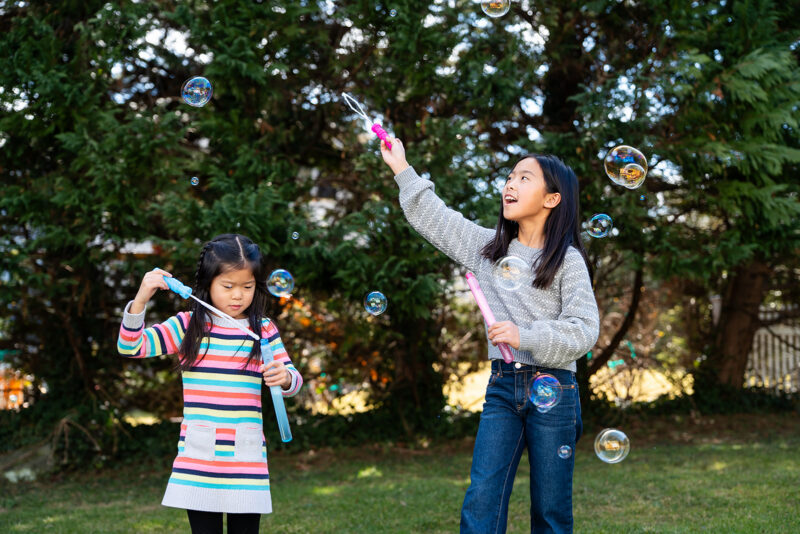 Two young girls playing with bubble wands during an outdoor portion of a family photo session.